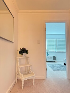 A hallway with a white console table and a potted plant, leading to a room with a white cabinet and a grey sofa. - Enjoyable townhome  (Alexandria)