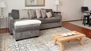Ein Wohnzimmer mit grauem Sofa, gemusterten Kissen, einem Holztisch und einem Teppich mit Muster.