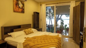 A bedroom with a bed, nightstands, a wooden wardrobe, and a sliding glass door leading to a balcony with potted plants.