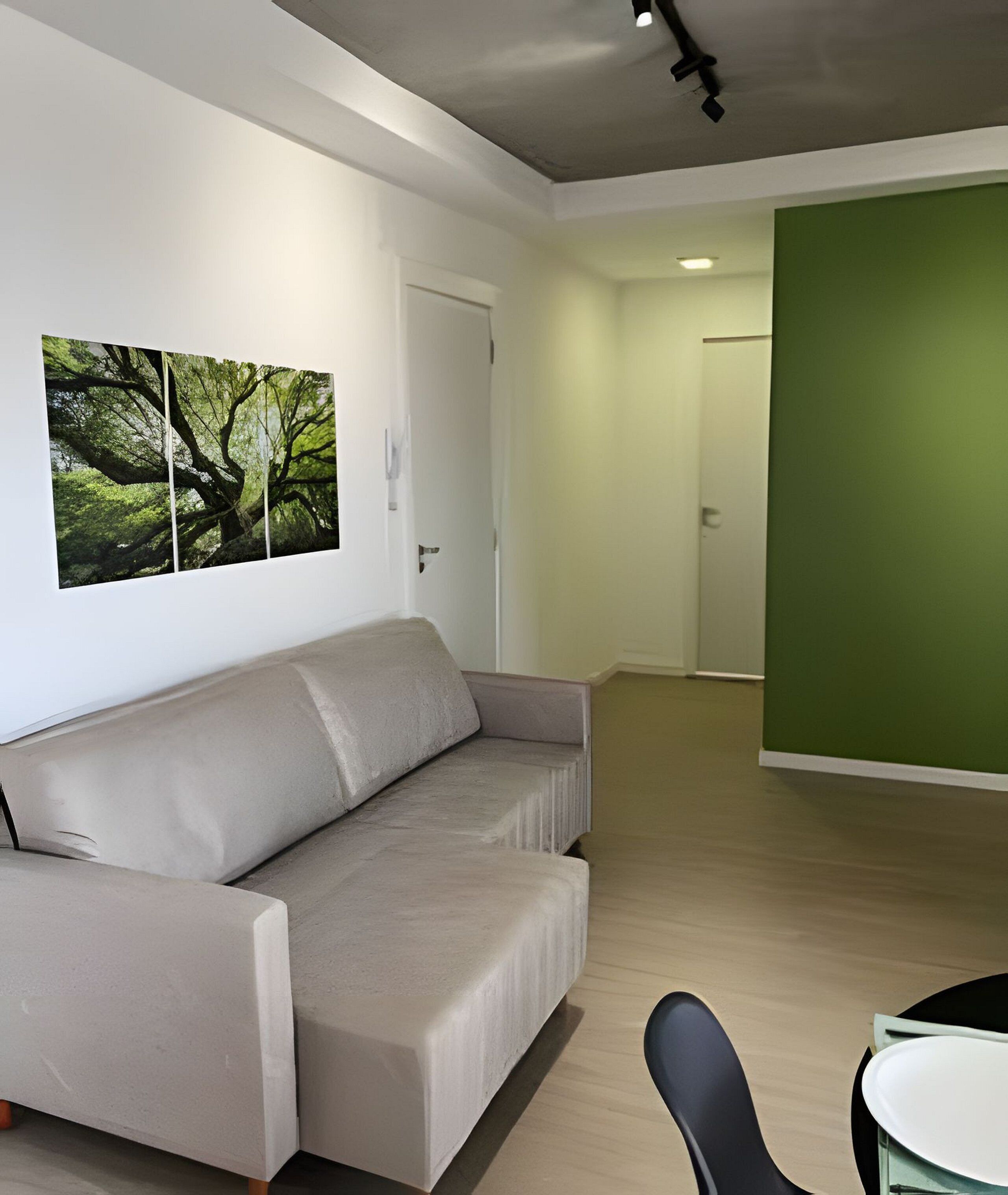 A modern living room with a beige sofa, a green accent wall, and a large nature-themed artwork on the wall.
