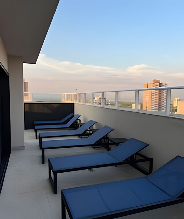 A rooftop terrace with multiple sun loungers aligned along the railing, overlooking a cityscape. - Aptos no Centro com Piscina e Academia (Maringá)