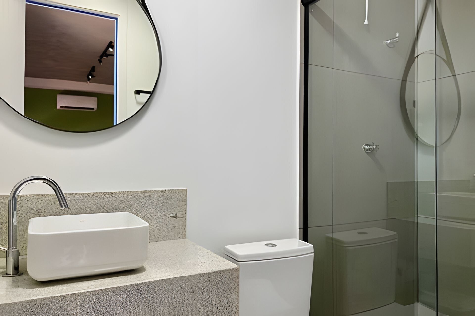 Um banheiro moderno com pia retangular, vaso sanitário e chuveiro com box de vidro.