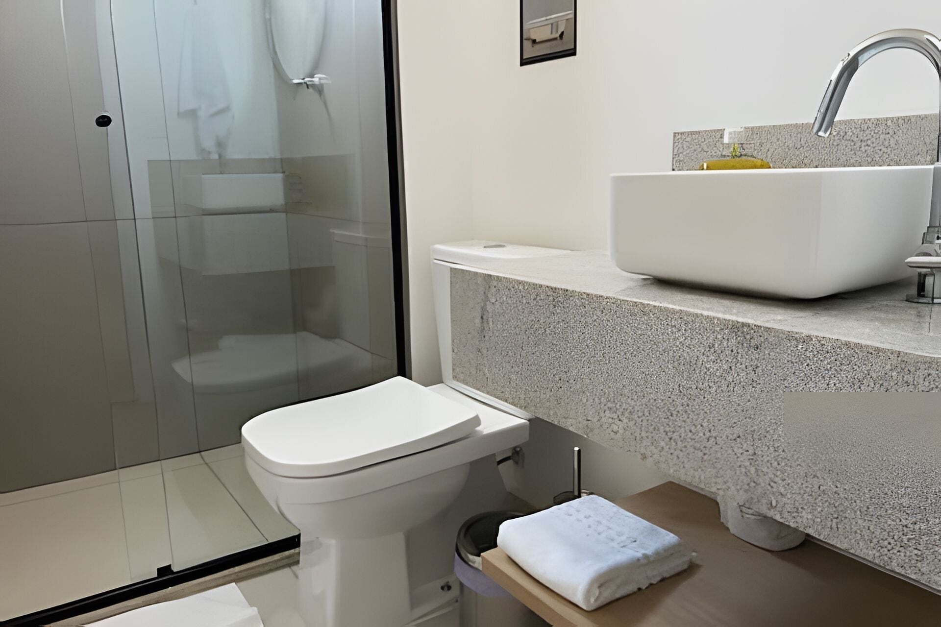 Un baño moderno con cabina de ducha de vidrio, inodoro blanco y encimera de granito con lavamanos.