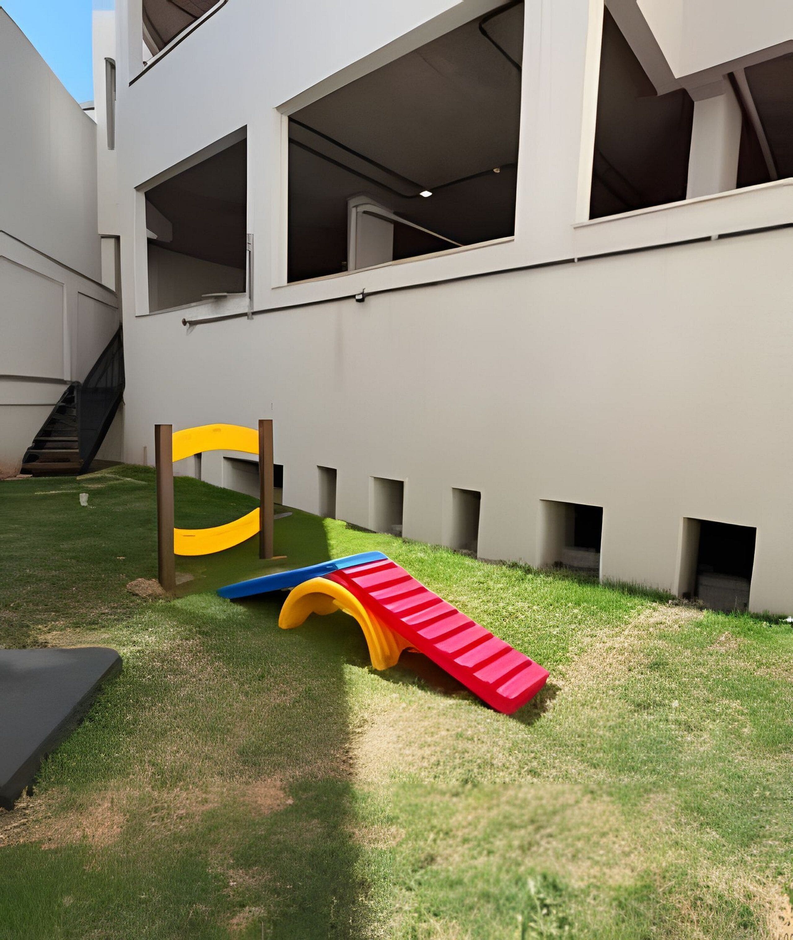 Une aire de jeux avec un toboggan et une structure d’escalade, située dans une cour intérieure avec un bâtiment en arrière-plan.