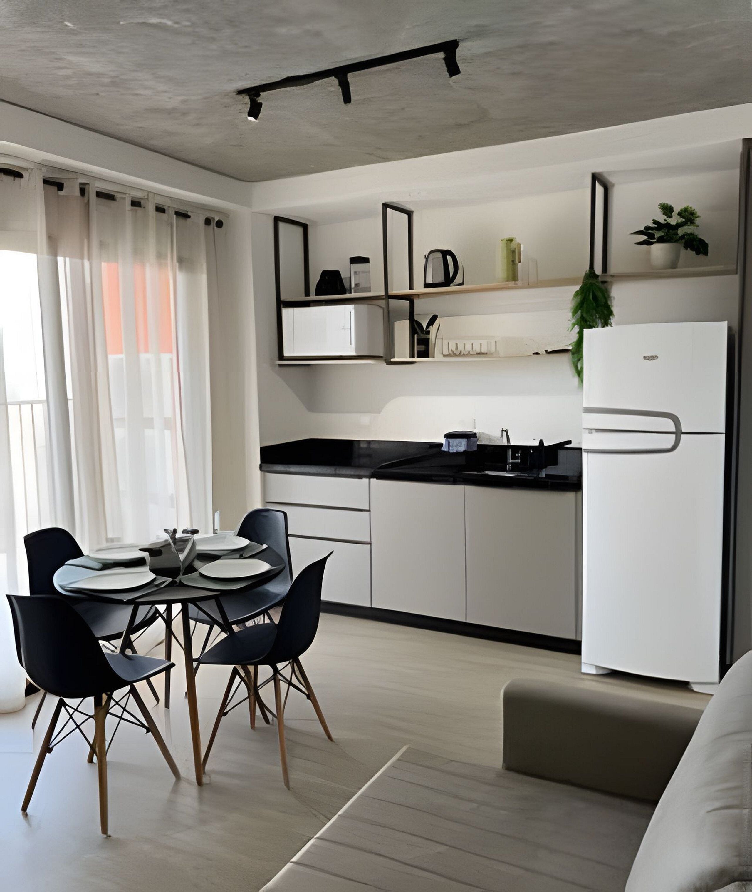 Una cocina moderna con comedor, con encimera negra, armarios blancos y refrigerador blanco.