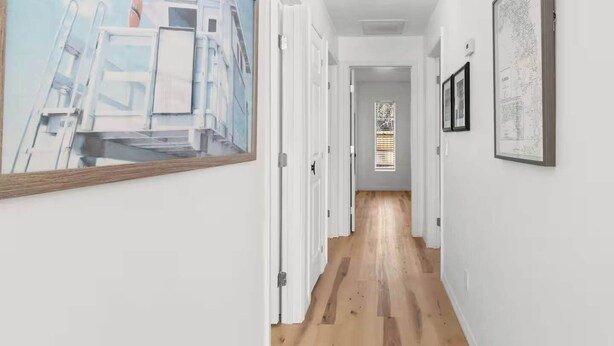 Un couloir aux murs blancs, au plancher en bois et aux œuvres d’art encadrées.