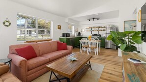 Un salon moderne comprenant un canapé, une table basse et un coin repas. On y trouve également une cuisine avec des meubles verts et un réfrigérateur.