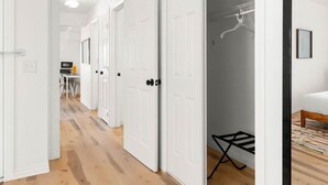 Un couloir avec des portes blanches menant à une chambre à coucher équipée d’un lit et d’un portant à vêtements.