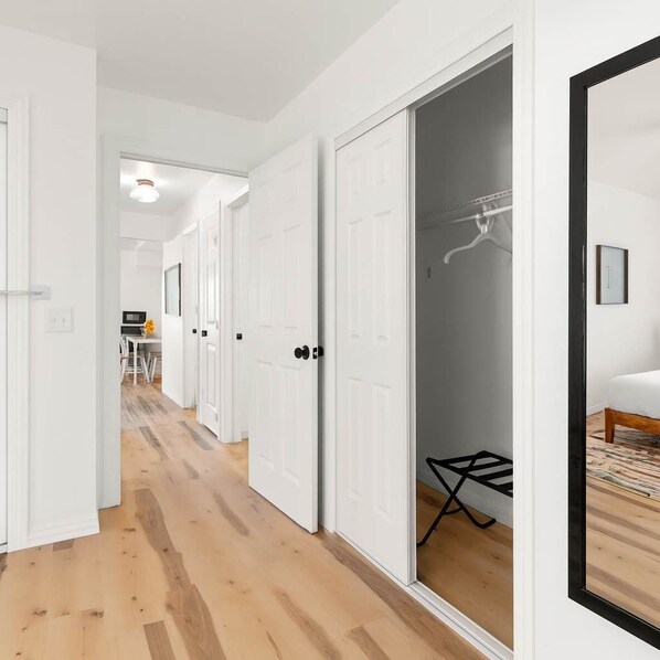 Un pasillo con puertas blancas que dan a un dormitorio con cama y perchero.