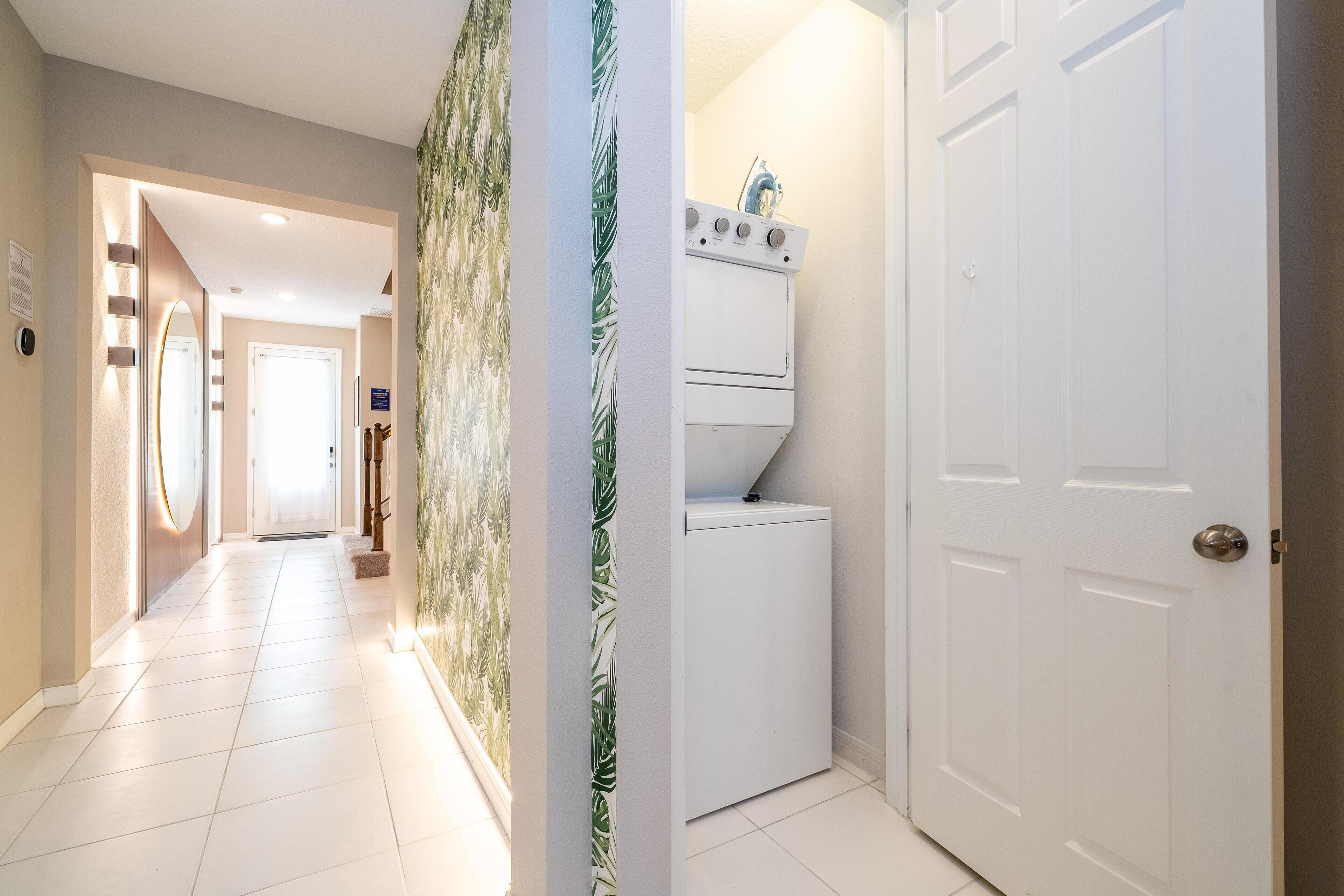 A hallway with a white door, a washing machine, and a wall with a leaf pattern.