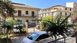 A residential building with multiple balconies, a gated entrance, and a parked car.