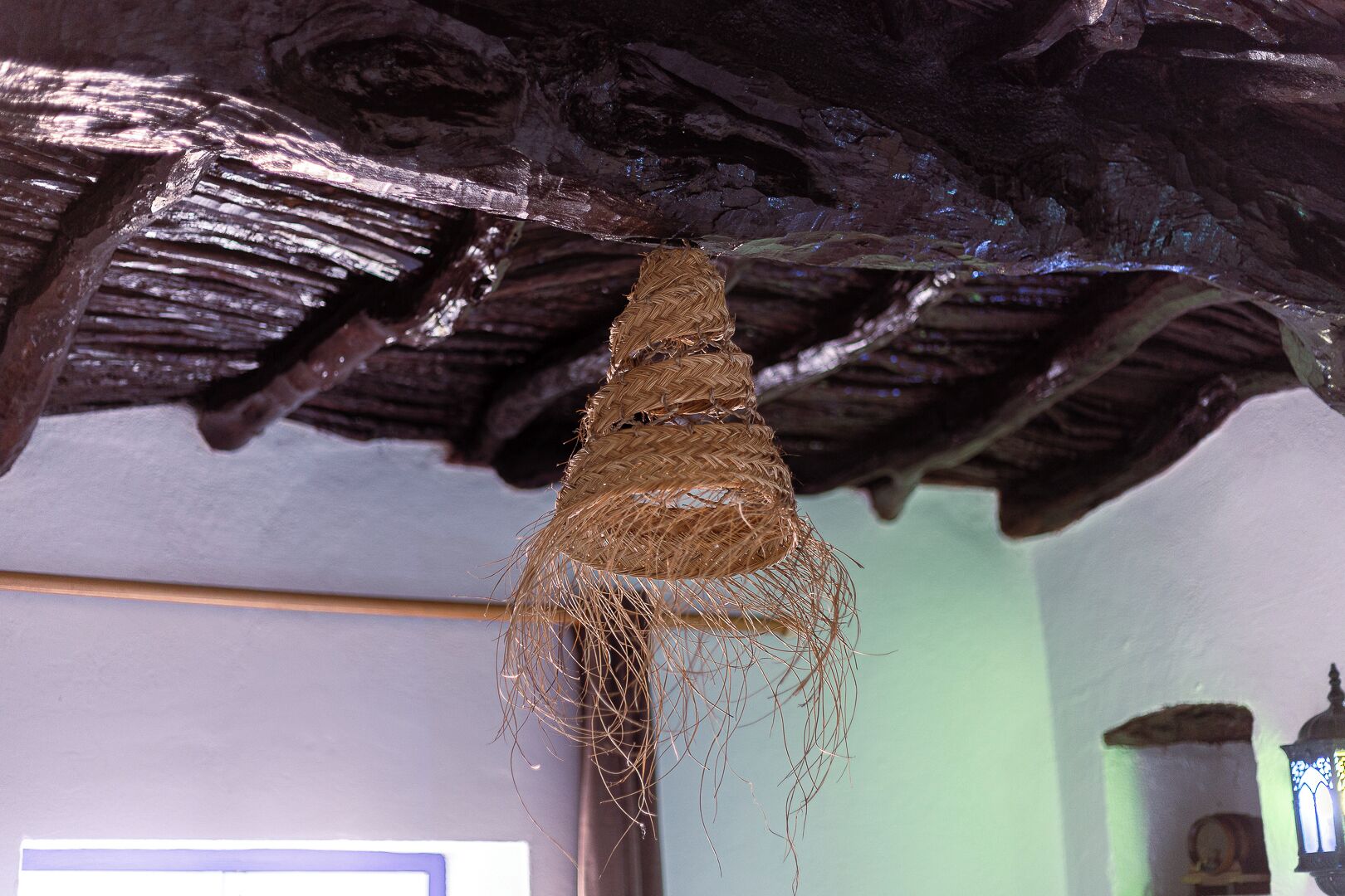 Un plafond rustique avec des poutres apparentes et un panier tressé suspendu.