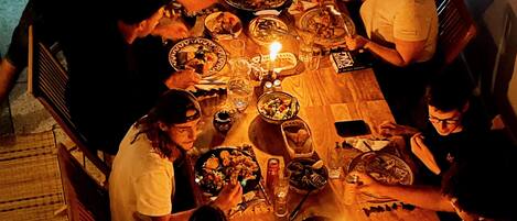 A group of people seated around a long wooden dining table with various dishes and glasses, illuminated by candles.