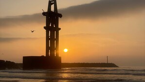 Un coucher de soleil sur la côte, avec une structure se détachant en silhouette sur le ciel.