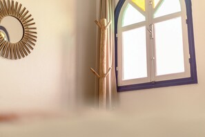 Una habitación con ventana, puerta de madera y espejo fijado a la pared.