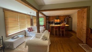 A cozy living room with a sofa, a small table, and a kitchen area in the background. - Cozy 3 bd, 8 min North Side Tremblant ski lifts (Lac-Supérieur)