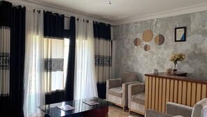 A modern living room with a glass-top coffee table, beige armchairs, and a wooden side table with a vase of flowers. - Peaceful, quiet 4-bedroom holiday home @Karambi, Fort Portal Tourism City Uganda (Fort Portal Tourism City)