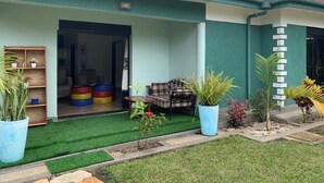A house with a green exterior, a red roof, and a porch area with a bench and potted plants. - Peaceful, quiet 4-bedroom holiday home @Karambi, Fort Portal Tourism City Uganda (Fort Portal Tourism City)