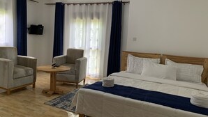 A hotel room with a bed, two armchairs, a small round table, and a TV mounted on the wall. - Peaceful, quiet 4-bedroom holiday home @Karambi, Fort Portal Tourism City Uganda (Fort Portal Tourism City)