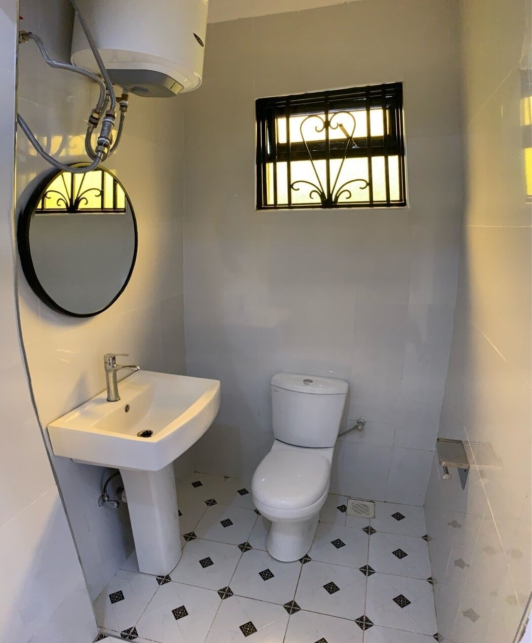 Un baño pequeño con un lavamanos blanco, un inodoro y una ventana con barrotes decorativos.