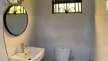 Un baño pequeño con un lavamanos blanco, un inodoro y una ventana con barrotes decorativos.