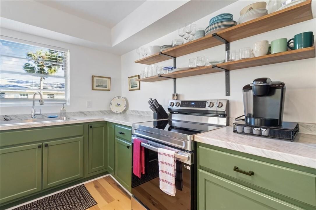 A kitchen with green cabinets, a stainless steel stove, a coffee maker, and shelves with dishes and glasses.