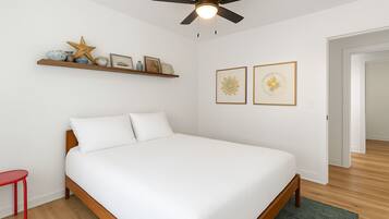 Un dormitorio con una cama, un ventilador de techo, una estantería con adornos y dos cuadros en la pared.