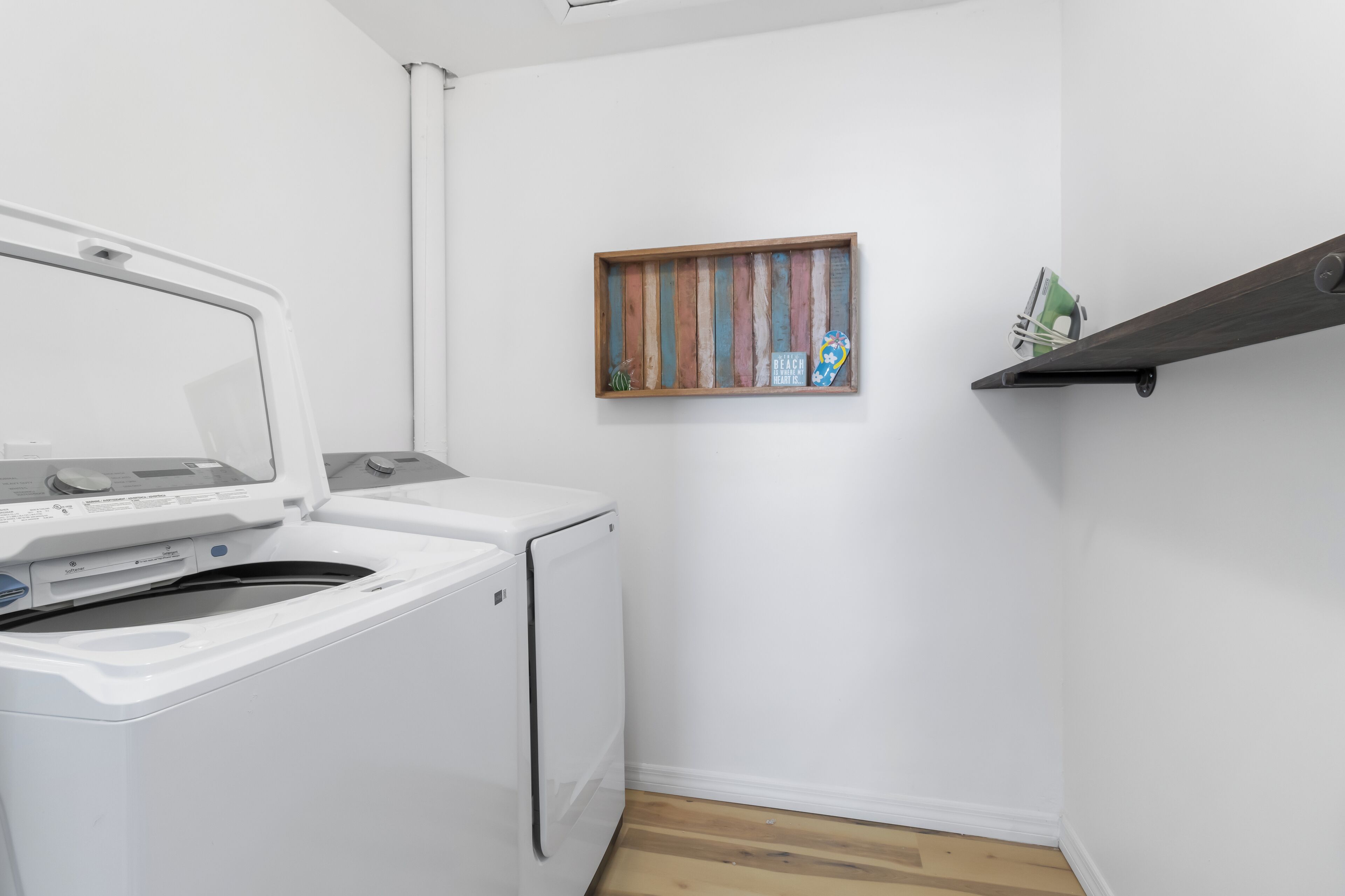 Un cuarto de lavado con lavadora y secadora, un estante de madera con objetos decorativos, y una ventana pequeña con vistas coloridas.