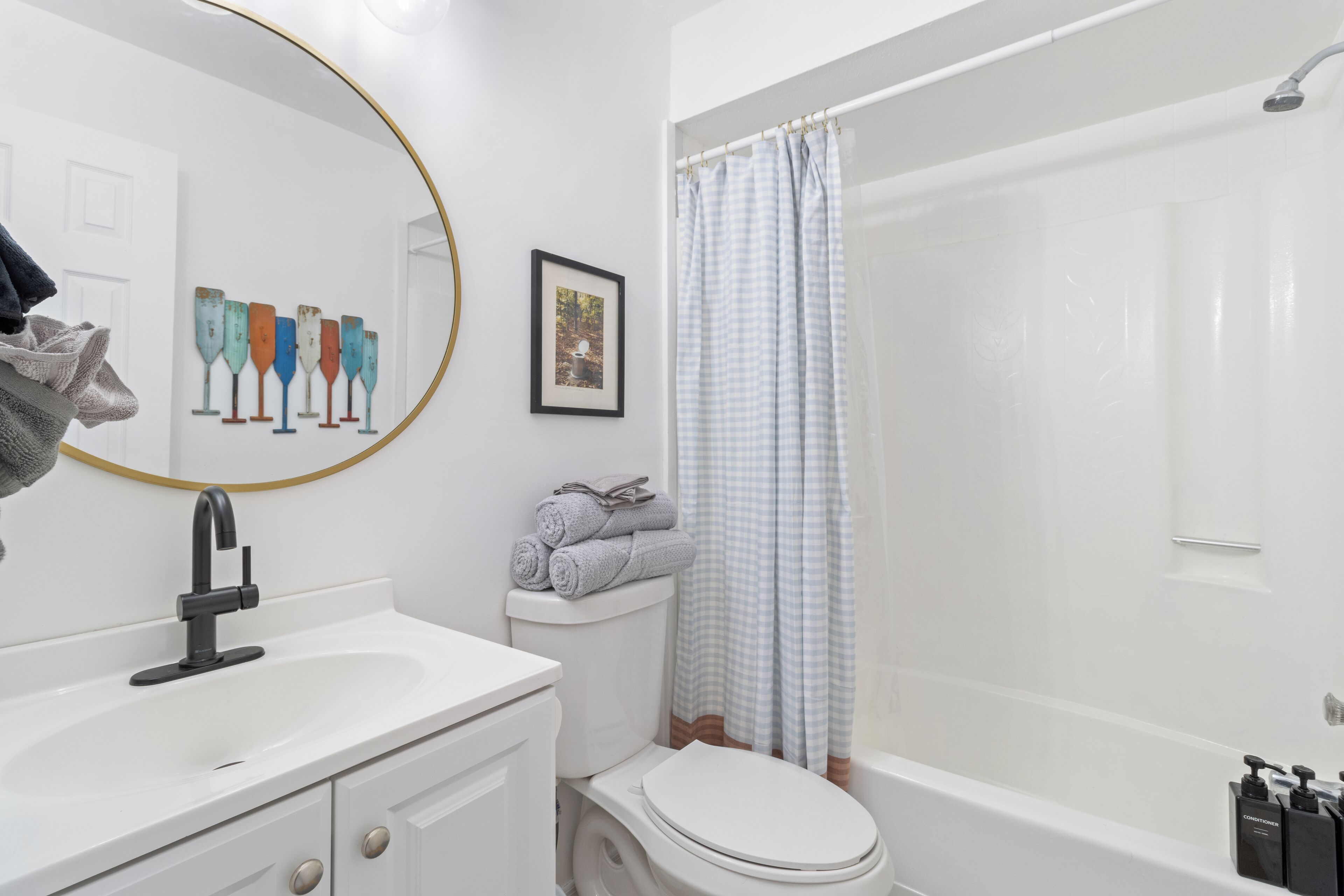 Un bagno con lavandino, water e vasca da bagno bianchi. C'è un porta asciugamani con asciugamani, un quadro incorniciato sulla parete e uno specchio con cornice dorata.