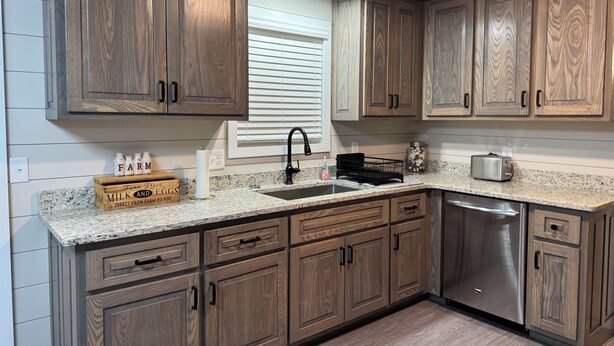 A kitchen with wooden cabinets, a granite countertop, a stainless steel dishwasher, and a window with blinds. - FARMHOUSE 89 (Bryant)