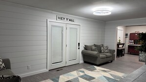 A modern living room with a sofa, a patterned rug, and a sign above the door that reads "HEY Y'ALL". - FARMHOUSE 89 (Bryant)