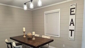 A dining area with a wooden table, white chairs, and a wall-mounted sign reading "EAT". - FARMHOUSE 89 (Bryant)