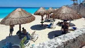 A beach with thatched umbrellas, sun loungers, and a stone wall. - Beach Front Flat!! (Cancún)
