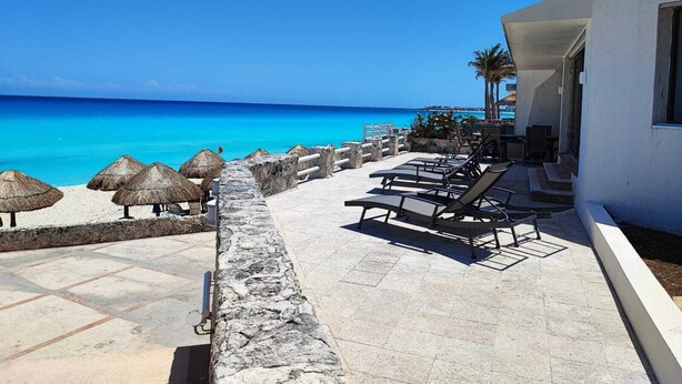 A beachside lounge with sun loungers and thatched umbrellas, overlooking a clear blue sea. - Beach Front Flat!! (Cancún)