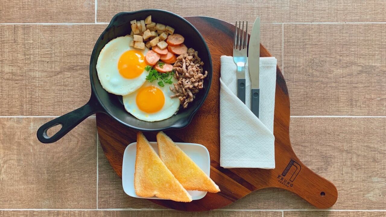 A breakfast plate with fried eggs, sausage, and hash browns on a wooden board.