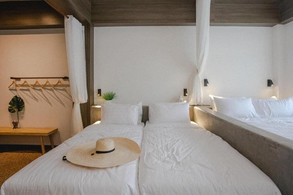A double bed with white linens, a straw hat, and a bedside table with a plant.