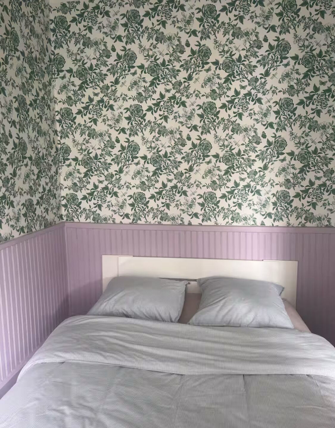 A bedroom with a bed, a headboard, and a floral wallpaper pattern.