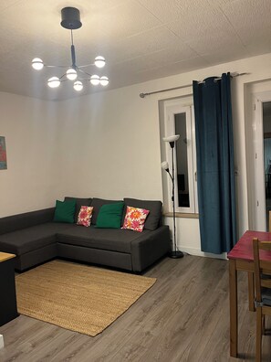 A living room with a sectional sofa, a floor lamp, a dining table with chairs, and a ceiling light fixture. - Weaver's house (36 m), full of charm in the center of Cholet, with garden. (Cholet)