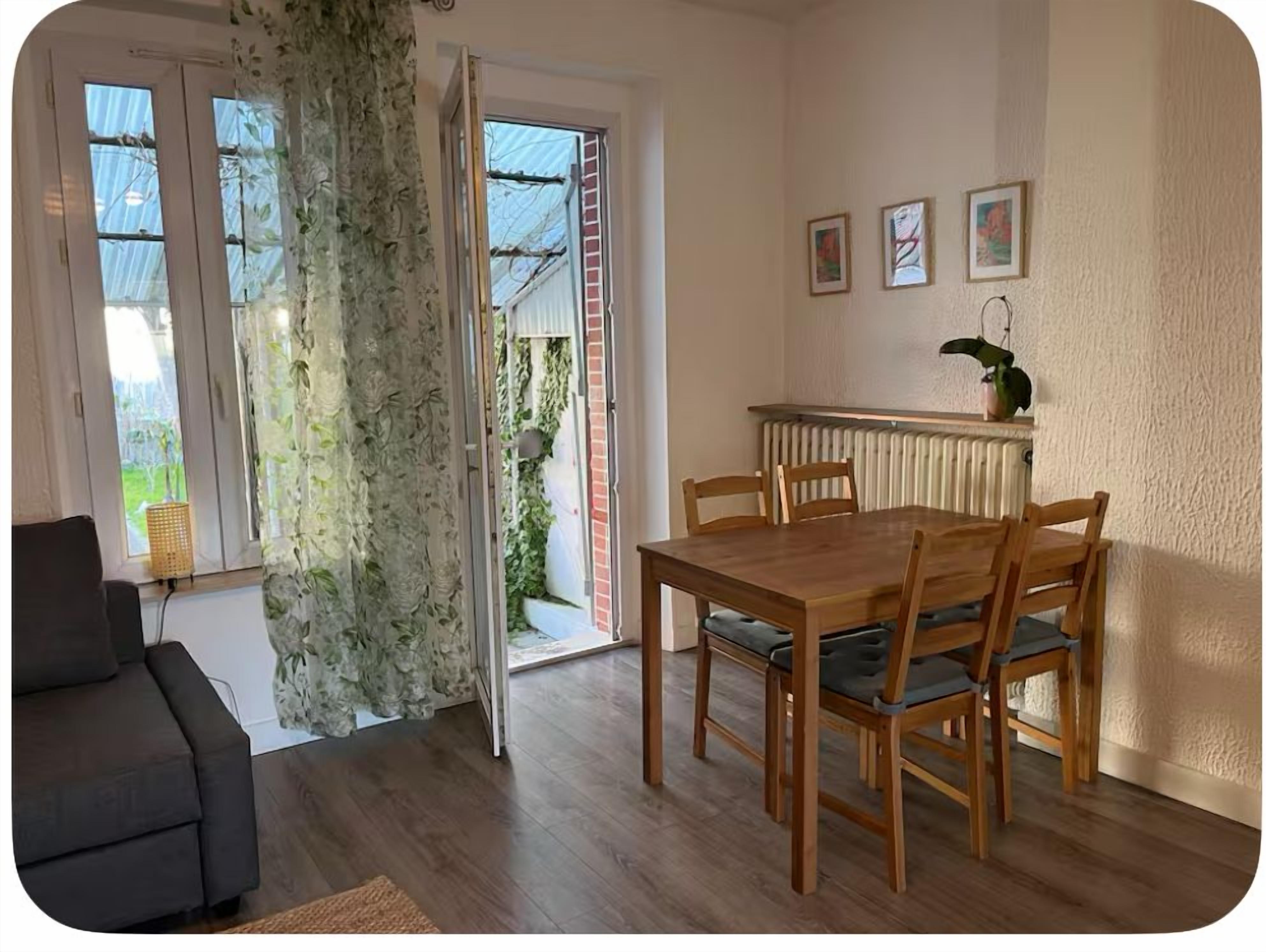 Comedor con mesa y sillas de madera, un radiador y vista a follaje por la puerta abierta.