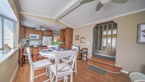 Una cocina moderna con armarios de madera, una isla central y un comedor con sillas blancas.