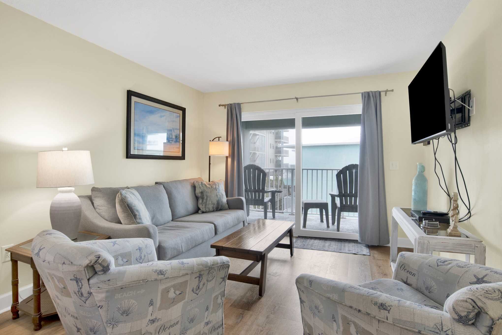 A living room with a sofa, armchairs, a coffee table, a TV, and a balcony with chairs.