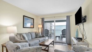 A living room with a sofa, armchairs, a coffee table, a TV, and a balcony with chairs. - Beachside Comfort | Steps to Sand + Heated Pool (Gulf Shores)