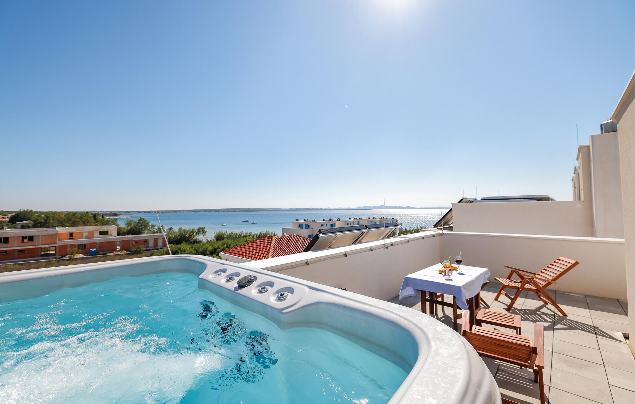 Ein Pool auf dem Dach mit Blick auf das Meer, ein Tisch mit Getränken und Holzstühle.