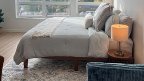 Une chambre à coucher avec un grand lit, deux fenêtres, une lampe de chevet et une vue sur le paysage urbain.