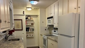 A kitchen with white cabinets, a granite countertop, a stainless steel sink, a microwave, an oven, and a refrigerator. - Mellon Camp. Charming riverside cabin. (Georgetown)