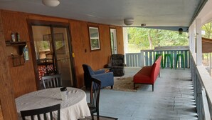 A covered patio area with a round table and chairs, a red bench, and a blue chair. - Mellon Camp. Charming riverside cabin. (Georgetown)