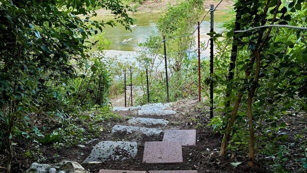 A stone pathway leading to a river, surrounded by lush greenery and trees. - Mellon Camp. Charming riverside cabin. (Georgetown)