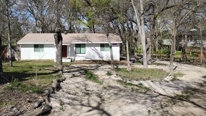 A small, single-story white house with a red door, surrounded by trees and a dirt path. - Mellon Camp. Charming riverside cabin. (Georgetown)