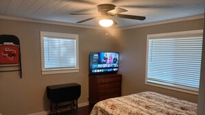 A bedroom with a bed, a TV on a dresser, a ceiling fan, and two windows with blinds. - Mellon Camp. Charming riverside cabin. (Georgetown)