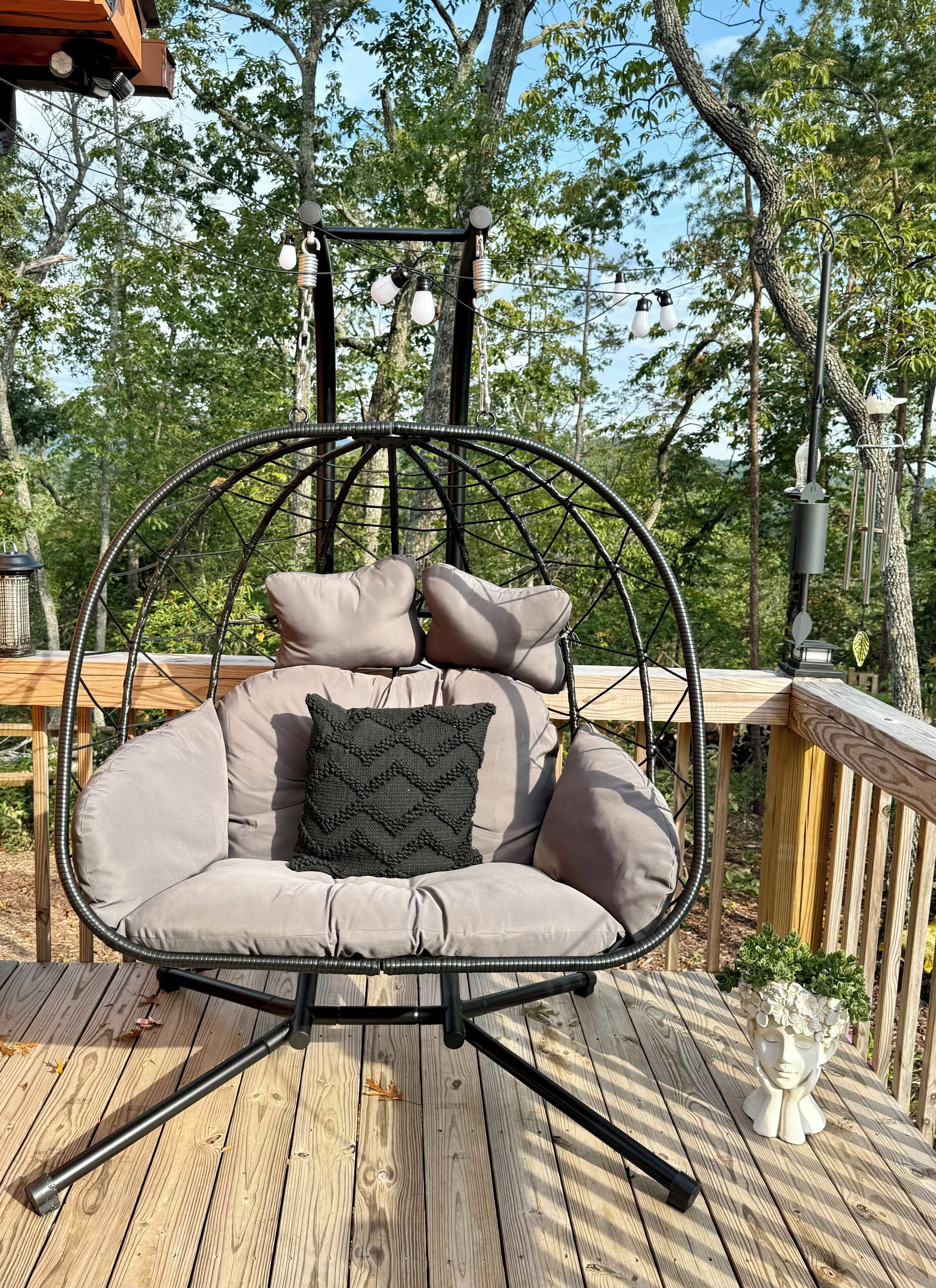 Una terraza de madera con una silla colgante que tiene asiento y respaldo acolchados, y un cabecero decorativo.